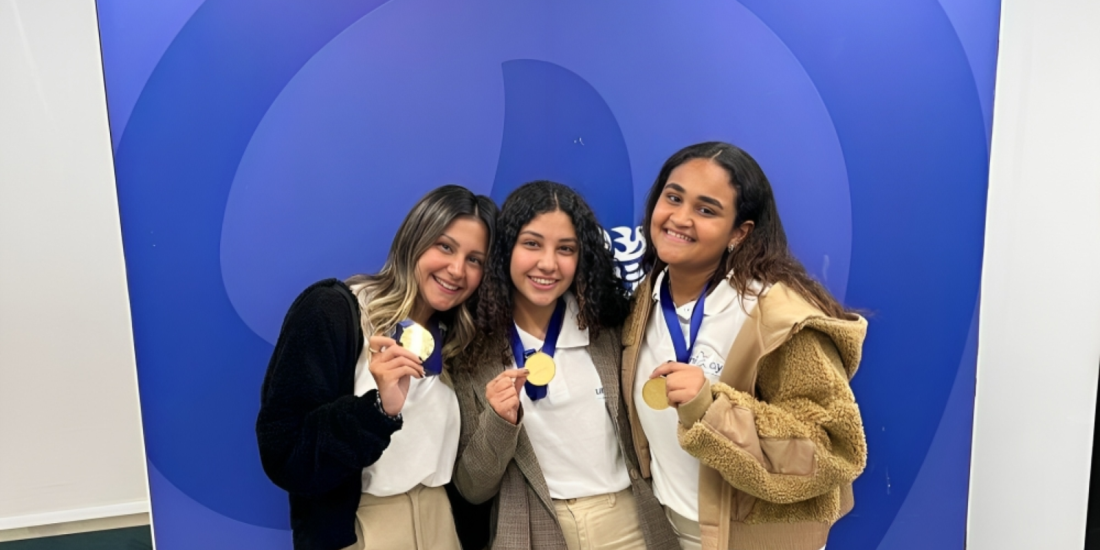 Three girls smiling wearing gold medals