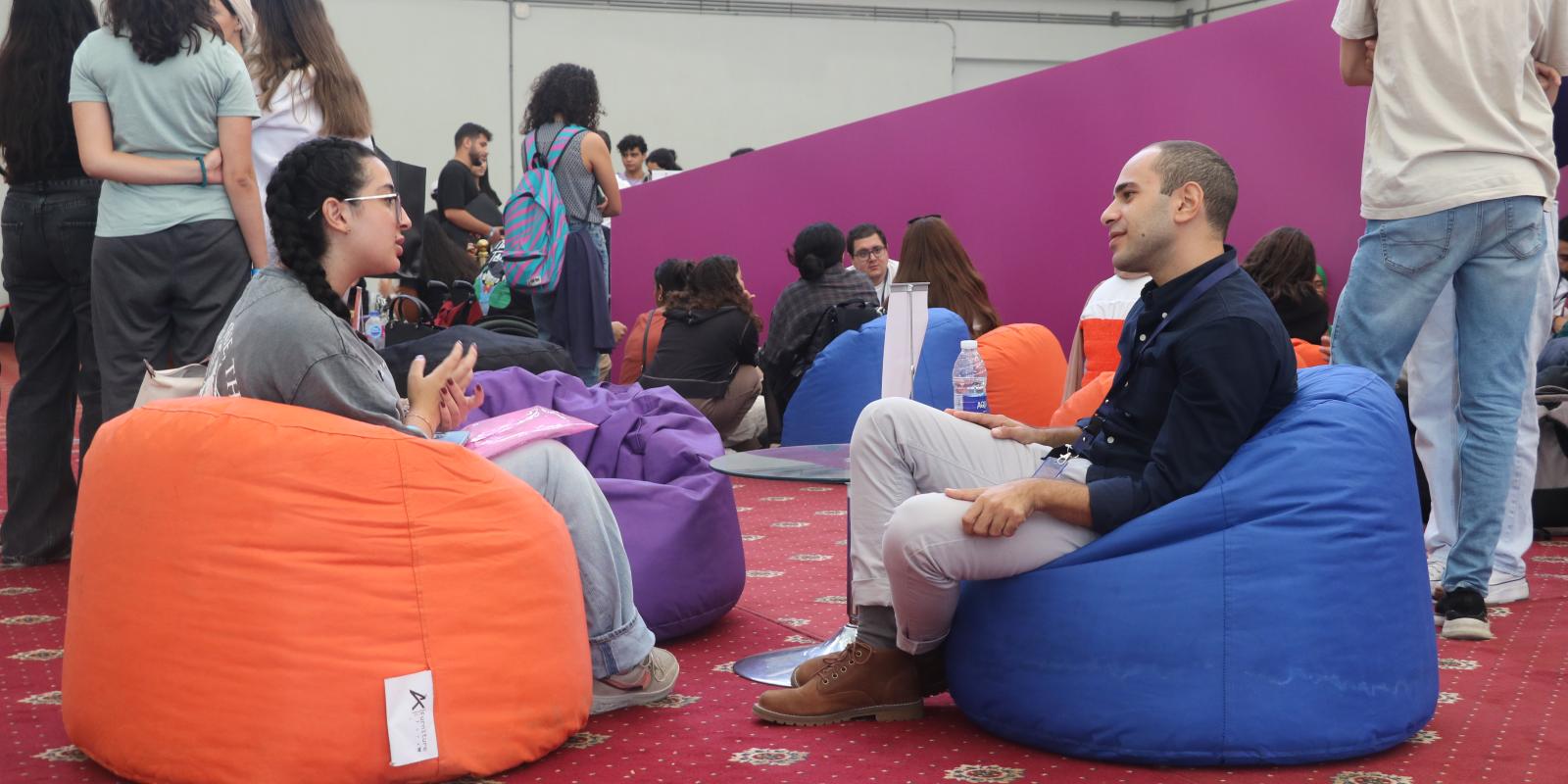 A girl and a boy talking to each other sitting on a bean bag