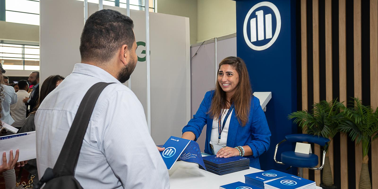 A girl standing in a booth give out a brochure to a man