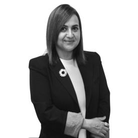 A black and white photo of a middle-aged woman smiling with her hands crossed.