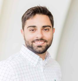 A middle-aged, fair-skinned man with brown hair and facial hear, smiling with his teeth and wearing a white button up shirt.