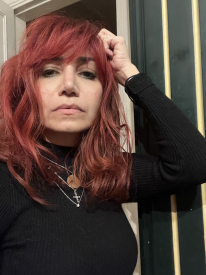 A middle-aged woman with red hair, posing in a selfie with her hand leaning on her head. 