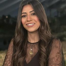 A young adult woman with brown, wavy hair, smiling towards the camera. 
