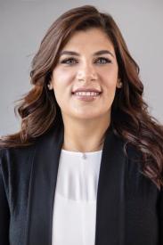 A middle-aged woman with brown hair, smiling in a professional photo with a black blazer and white shirt. 
