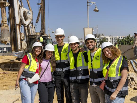 A group of girls and boys wearing safety vests and helmet on site