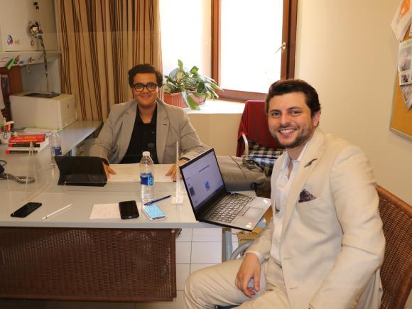 Two men sitting in an office on their laptops smiling